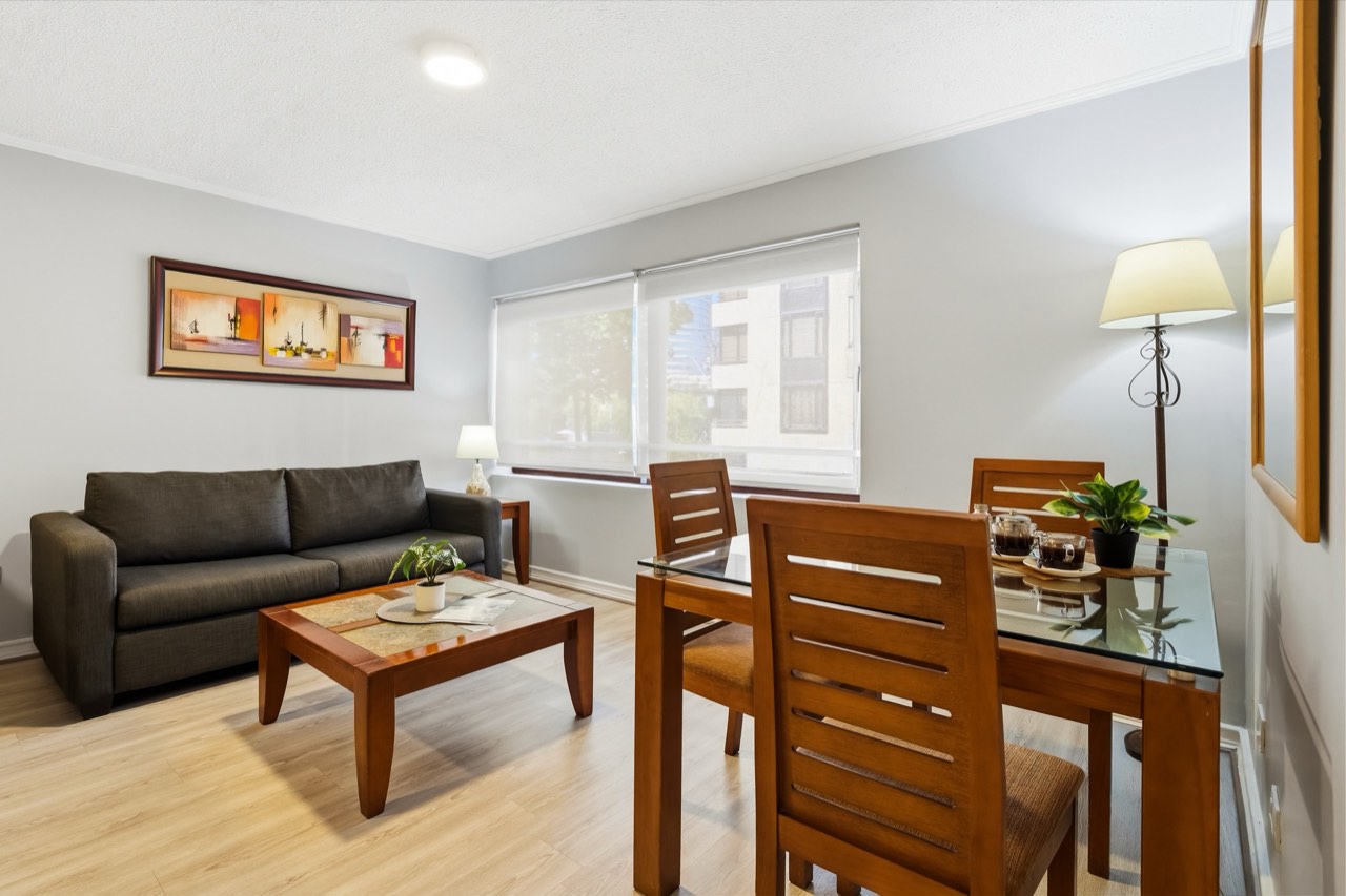 Living con sofá gris y comedor - Suite 106 Suites Vitacura