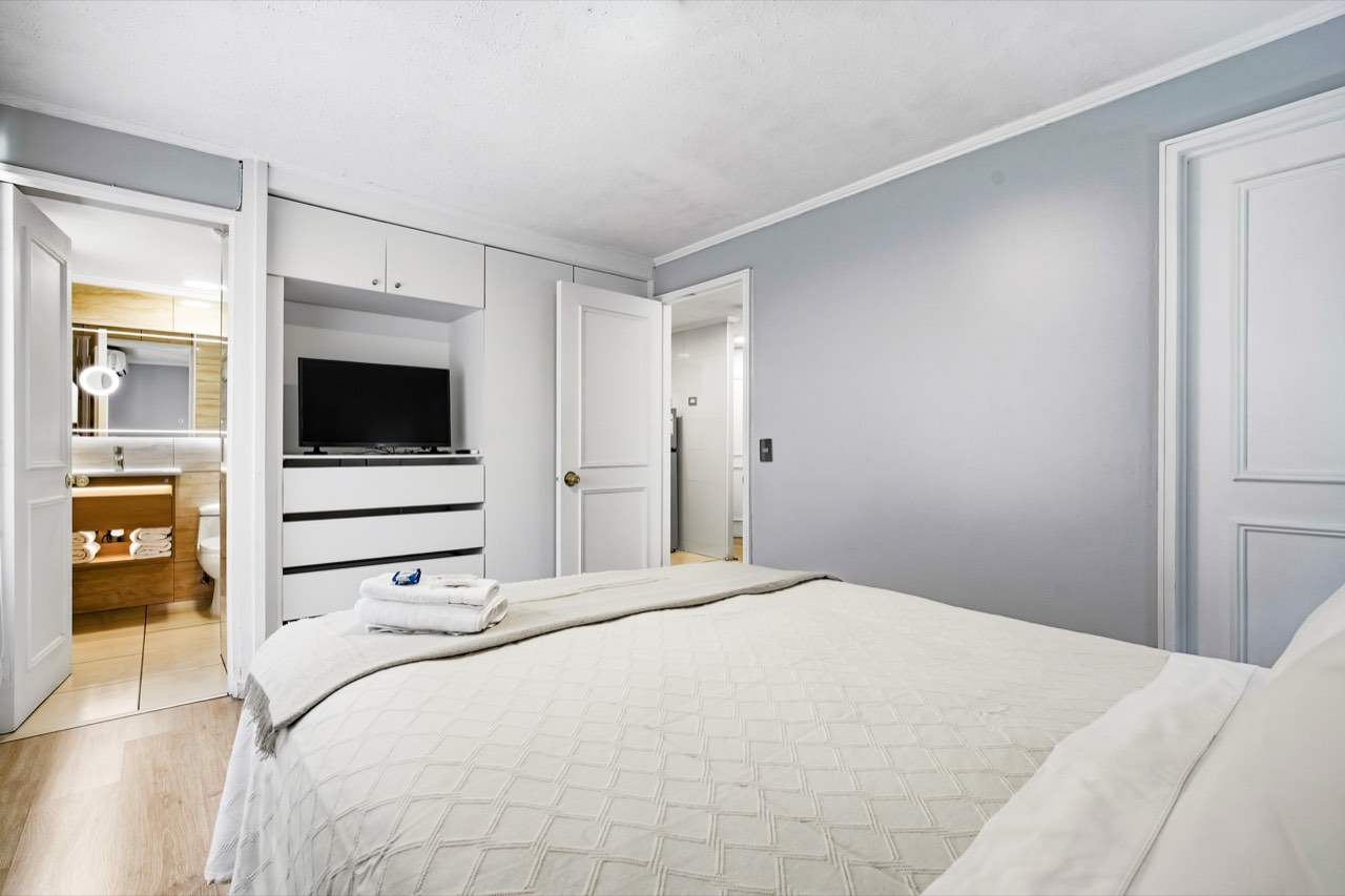 Dormitorio con TV y baño en suite - Suite 405 Suites Vitacura