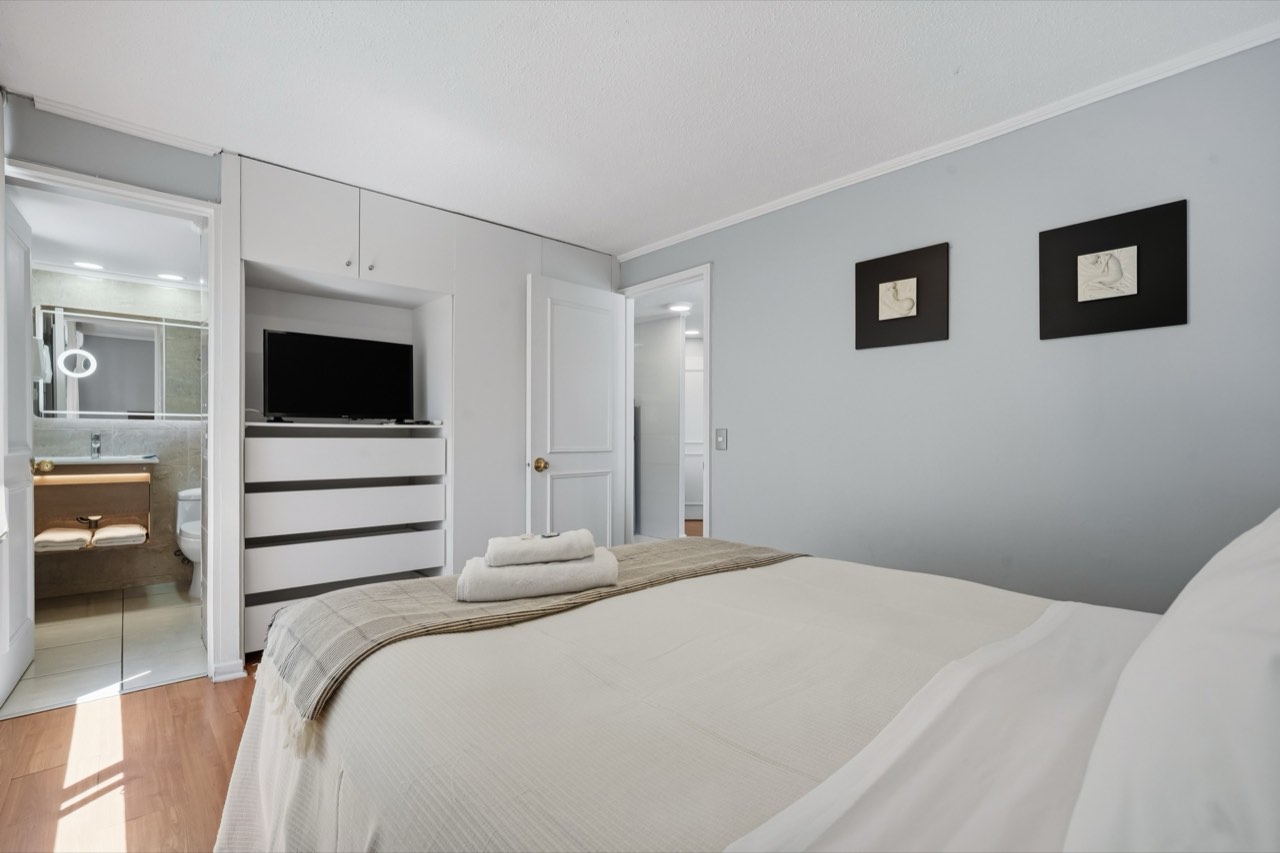 Dormitorio con TV y vista al baño - Suite 605 Suites Vitacura