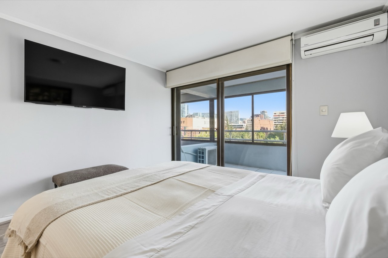 Dormitorio con TV y vista al balcón - Suite 801 Suites Vitacura